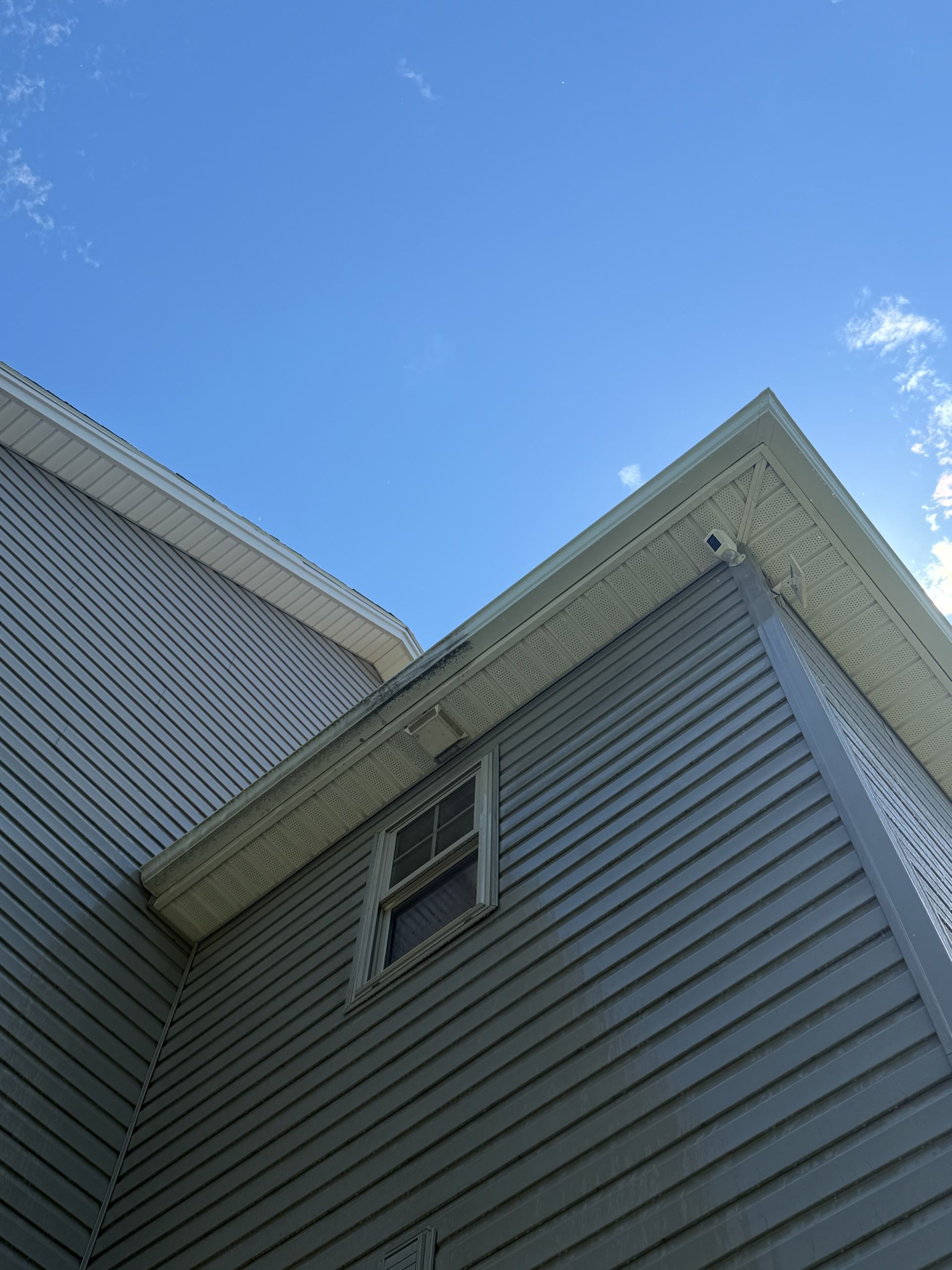 Gray house siding and a window beneath a roofline against a blue sky