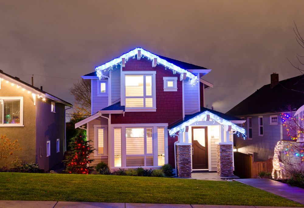 Suburban house at dusk outlined with blue holiday lights and warm glowing windows