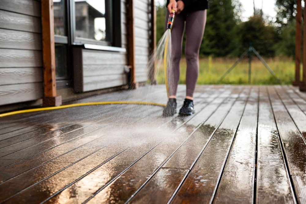 Person pressure-washing a wooden deck beside a house
