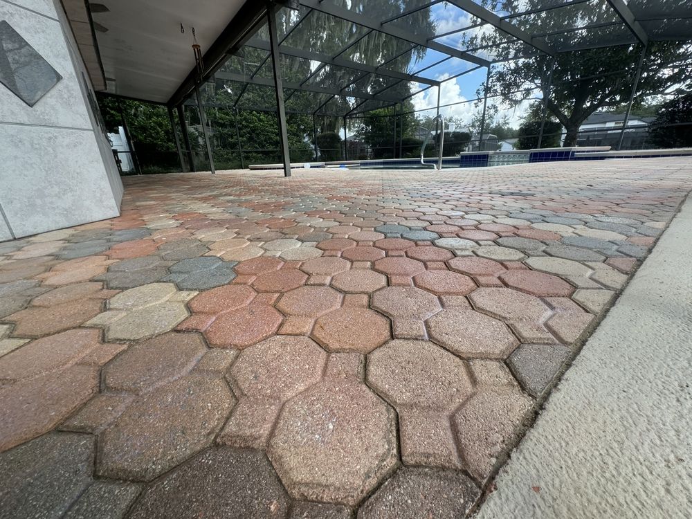 Hexagonal stone-paved walkway beside a building, with trees and benches in the background.