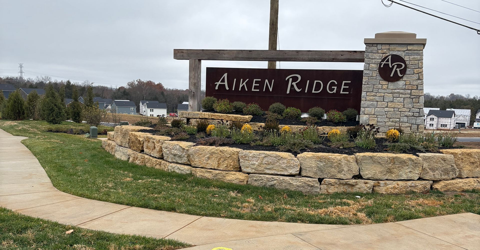 Neighborhood entrance monument with limestone boulder planter and stacked stone pillar