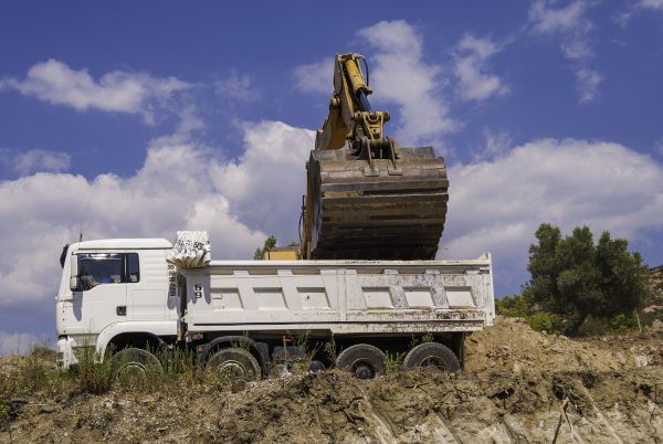 A dump truck is being loaded with dirt by an excavator.