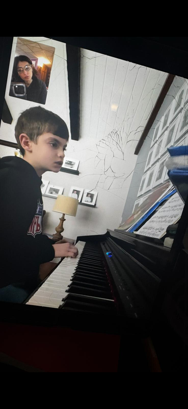 Child playing a black piano in a room, viewed from the side with a bright window nearby