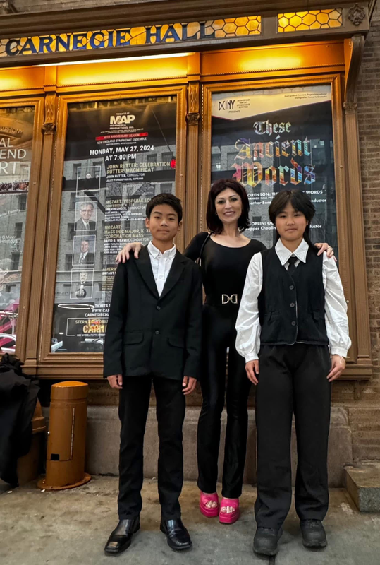 Three people standing outside Carnegie Hall entrance, with illuminated signage behind them.