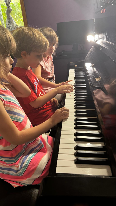 Two children playing a black piano, focused on the keys in a warmly lit room.