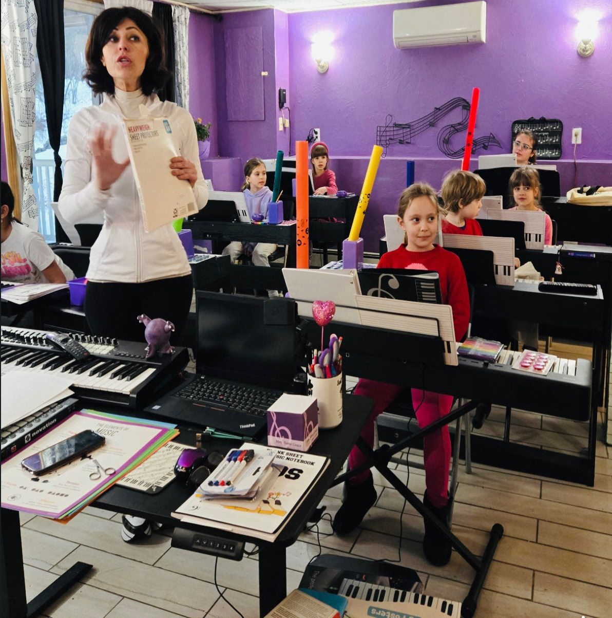 Teacher instructing students in a purple classroom with desks, laptops, and papers
