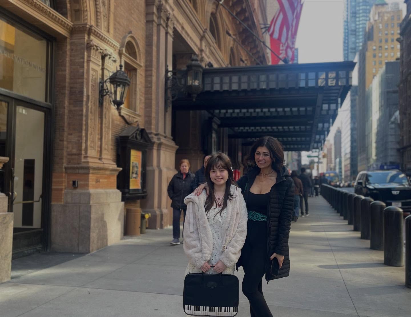 Two people standing on a city sidewalk outside a building with awning, one holding a suitcase