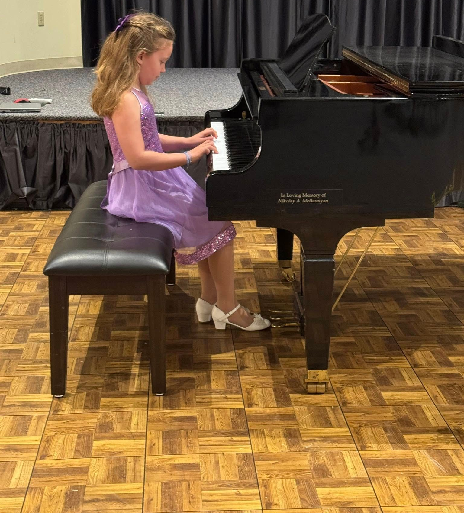Girl in a purple dress playing a black grand piano on a stage
