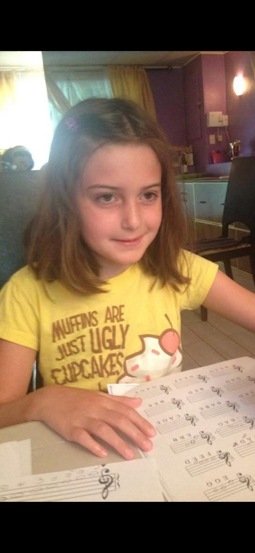 Girl in a yellow shirt writing on a worksheet at a table indoors