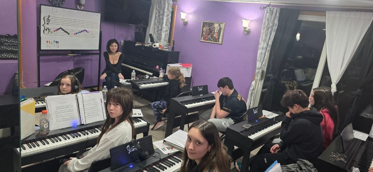 Group of students in a purple music classroom playing keyboards and listening to an instructor