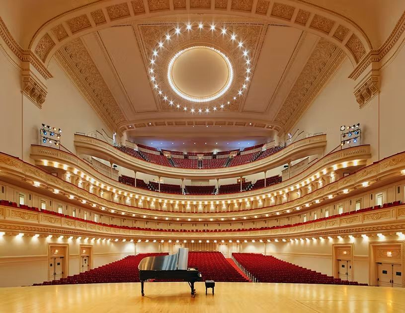 Grand concert hall with red seats, ornate balconies, and a grand piano on stage