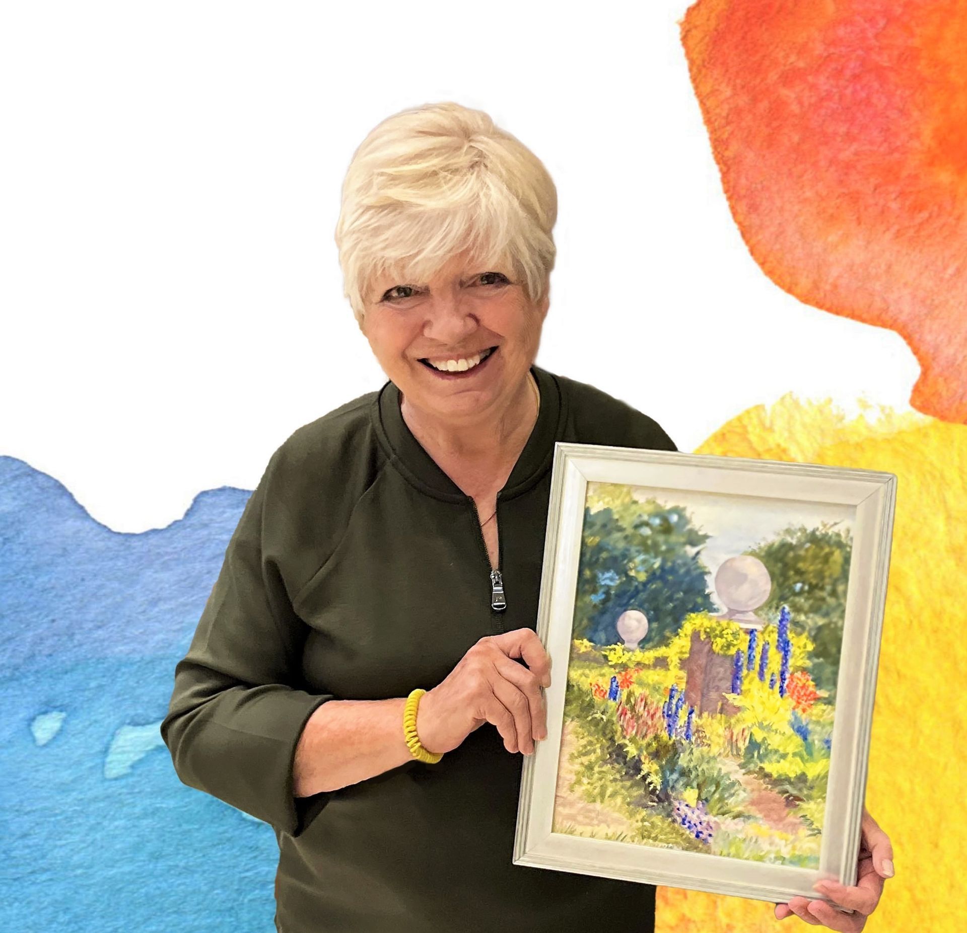 Woman with short blonde hair smiles, holding a framed watercolor painting of a garden scene; colorful abstract shapes in background.