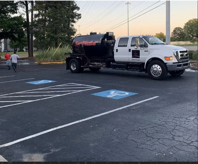 A worker uses a squeegee to apply black asphalt sealer to a driveway, with several buckets of sealant nearby.