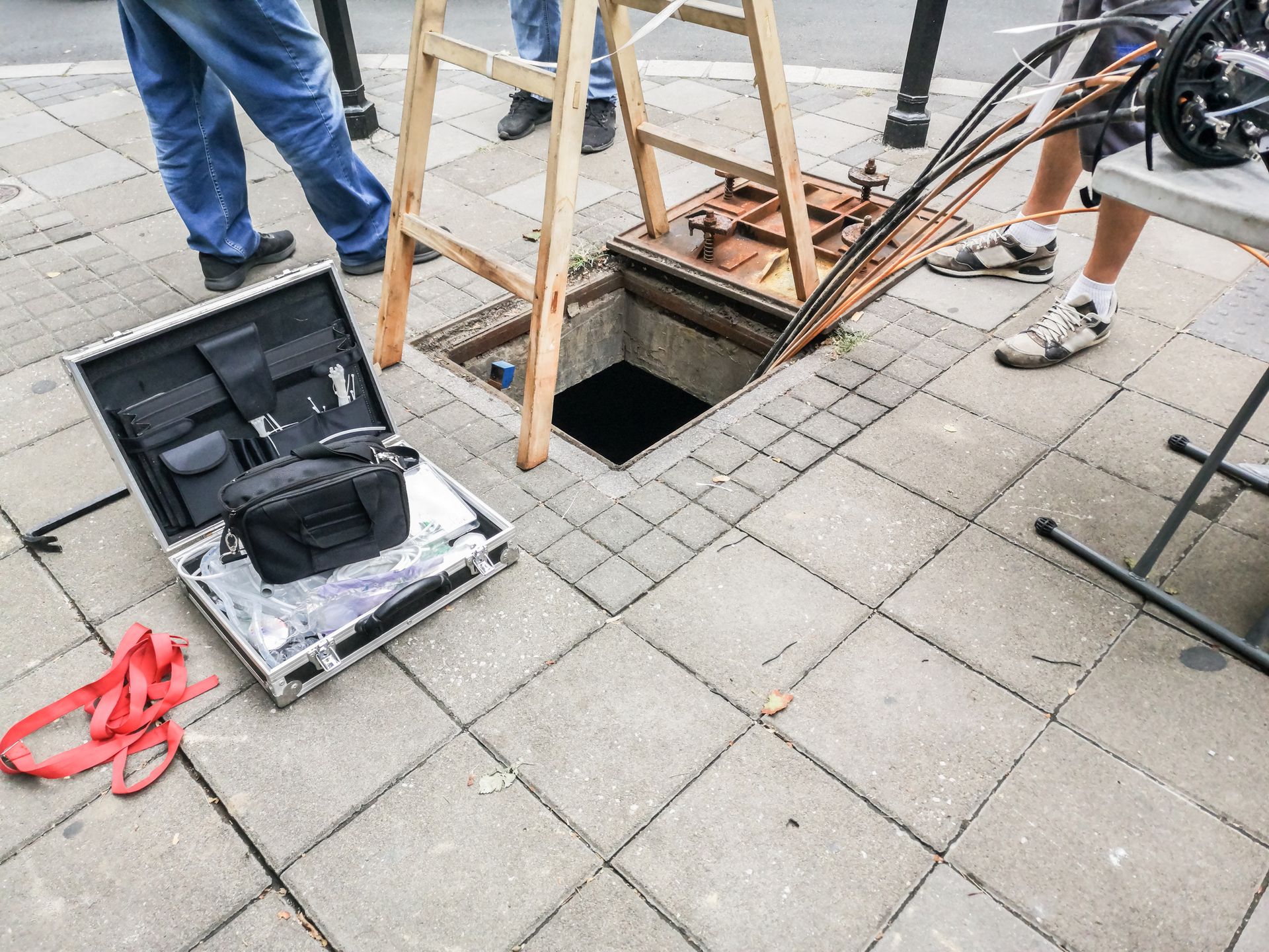 A manhole cover is being opened on a sidewalk next to a briefcase.