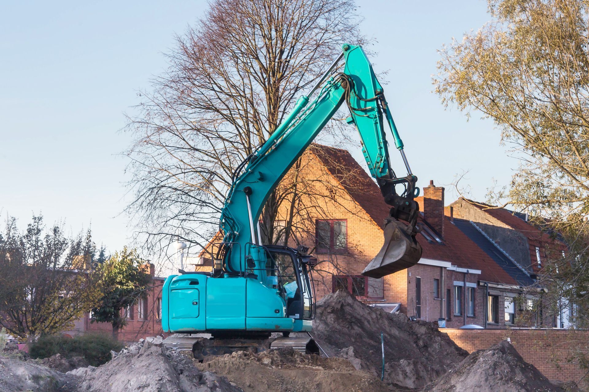 A blue excavator is digging a hole in the ground in front of a house.