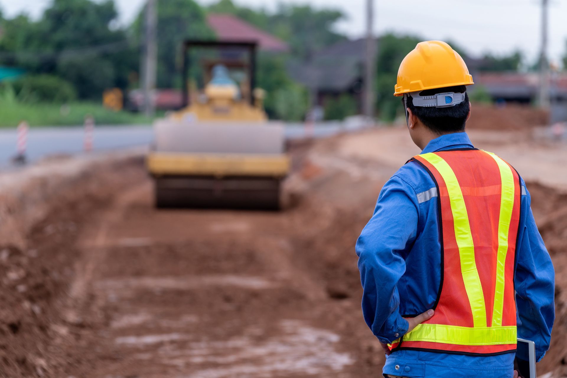 A construction worker is standing in front of a bulldozer at a construction site.