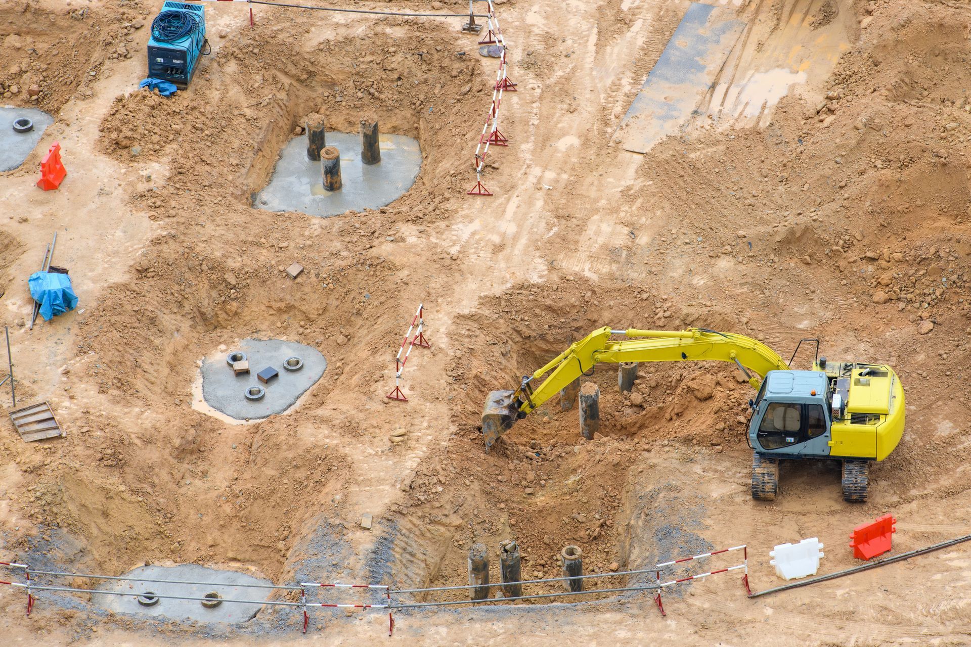 An aerial view of a construction site with a yellow excavator digging in the dirt.