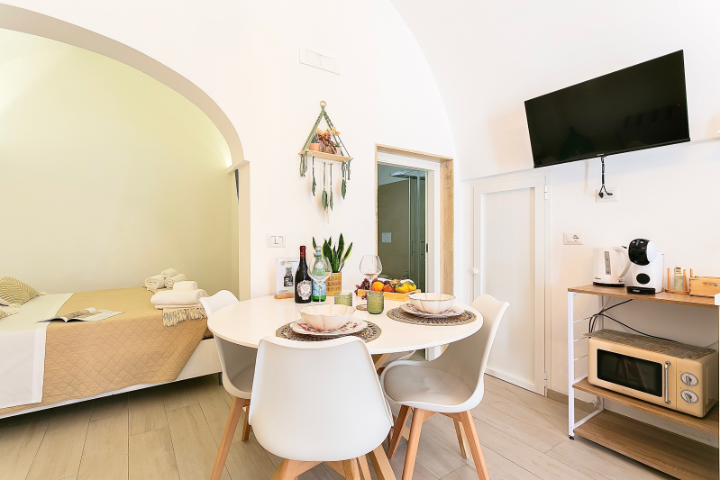 Zona pranzo con tavolo, sedie, TV, forno a microonde e letto in una nicchia ad arco.