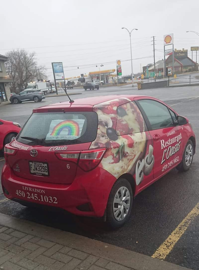 Une voiture rouge à motif pizza est garée dans une rue ornée d'un autocollant arc-en-ciel. Un numéro de téléphone est visible sur la voiture.