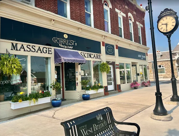 A storefront for Forrest Massage & Skincare with a street clock and a metal bench on a sunny sidewalk.