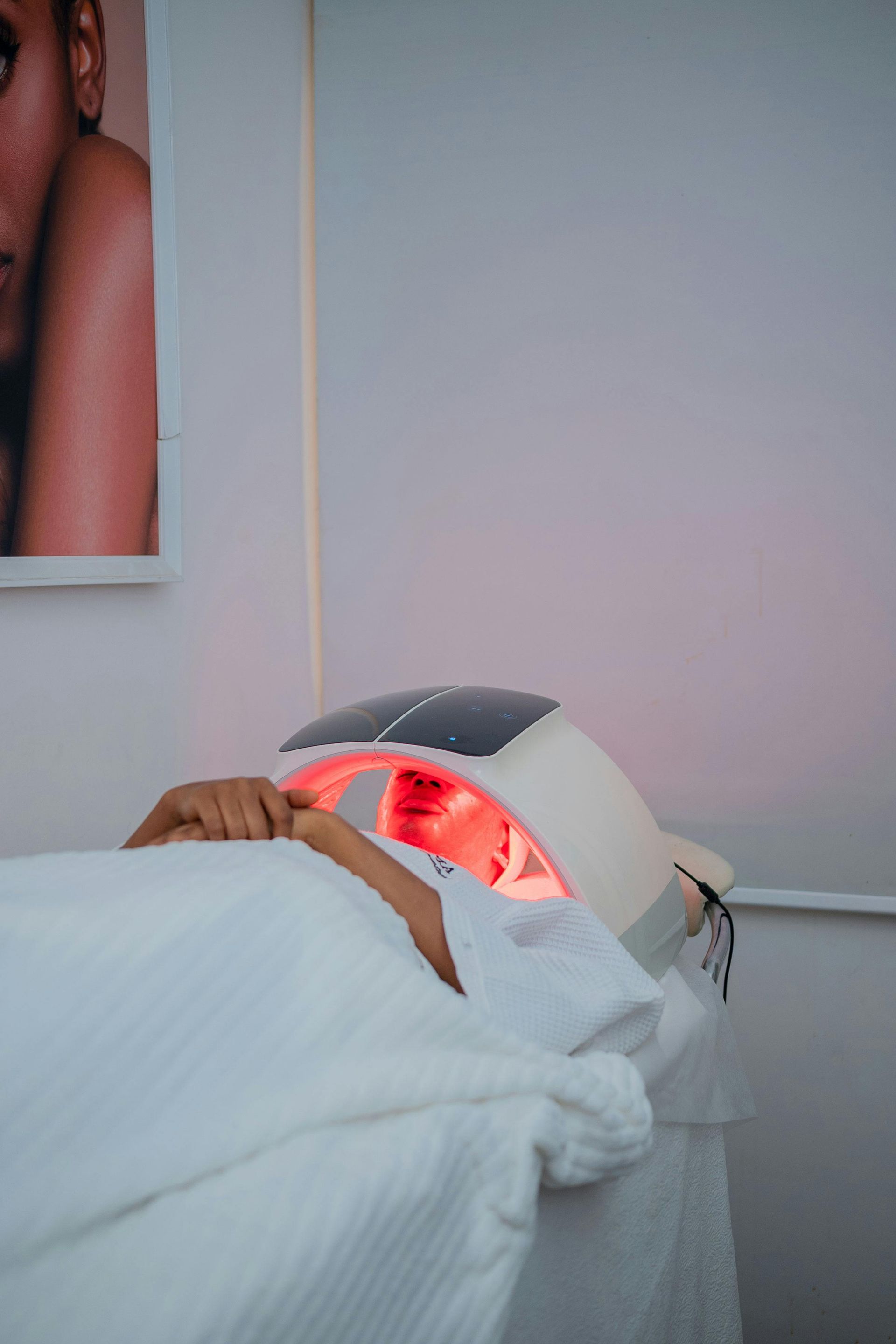 A person lying on a spa bed receives red light therapy treatment under a curved LED device.