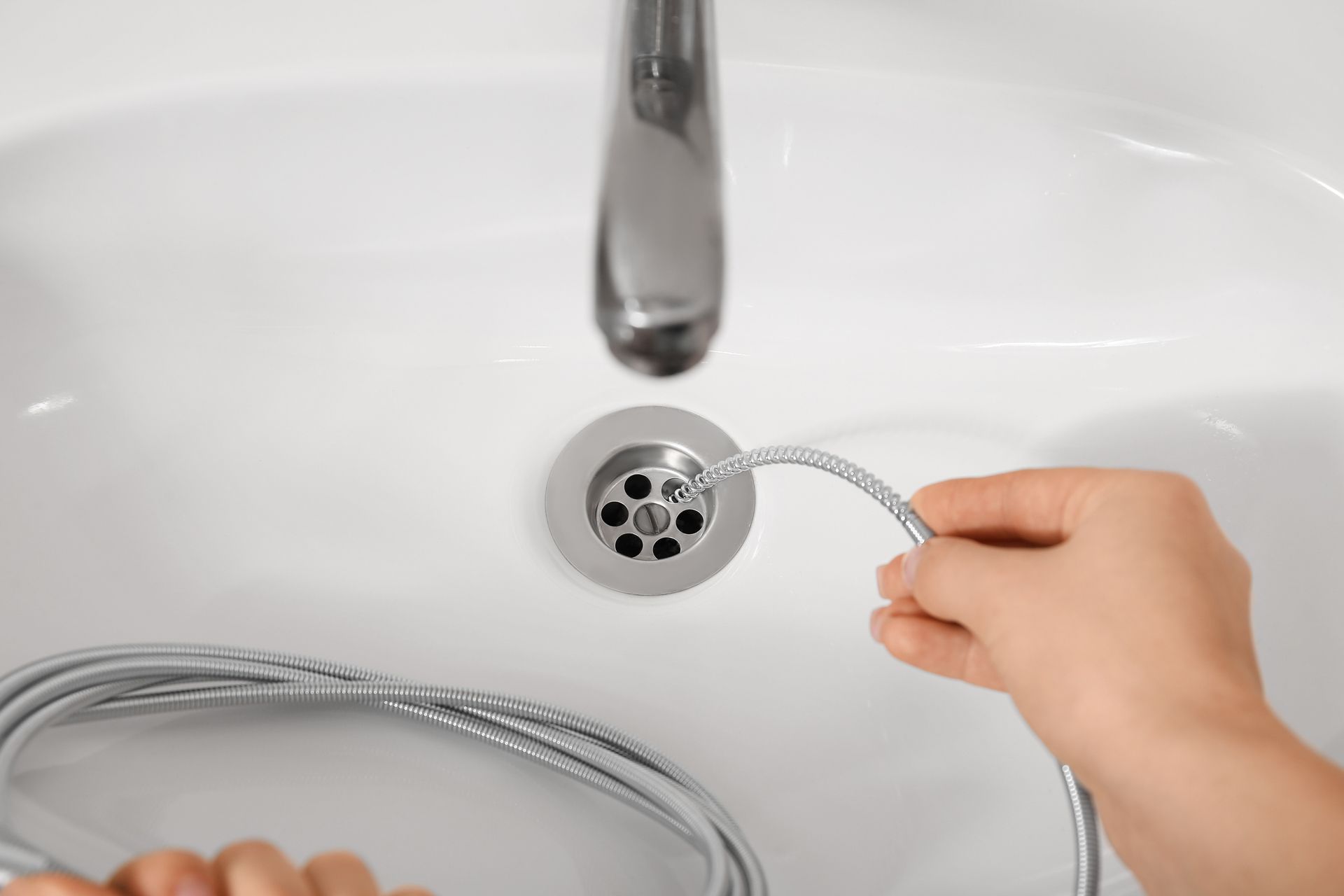 Hand holding a drain snake near a bathroom sink drain under a chrome faucet