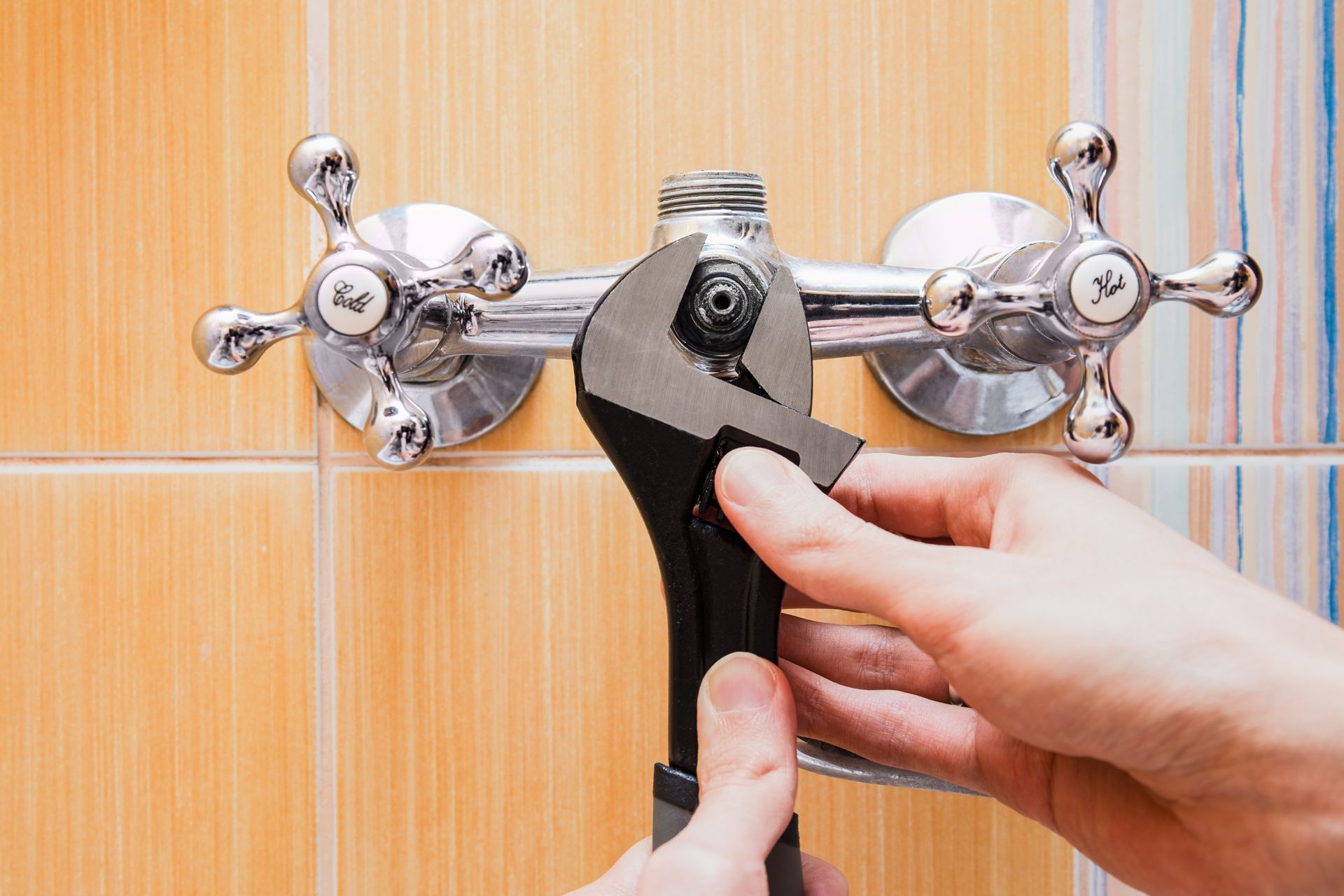 Hand tightening a black wrench on a chrome pipe fitting against orange tiled wall