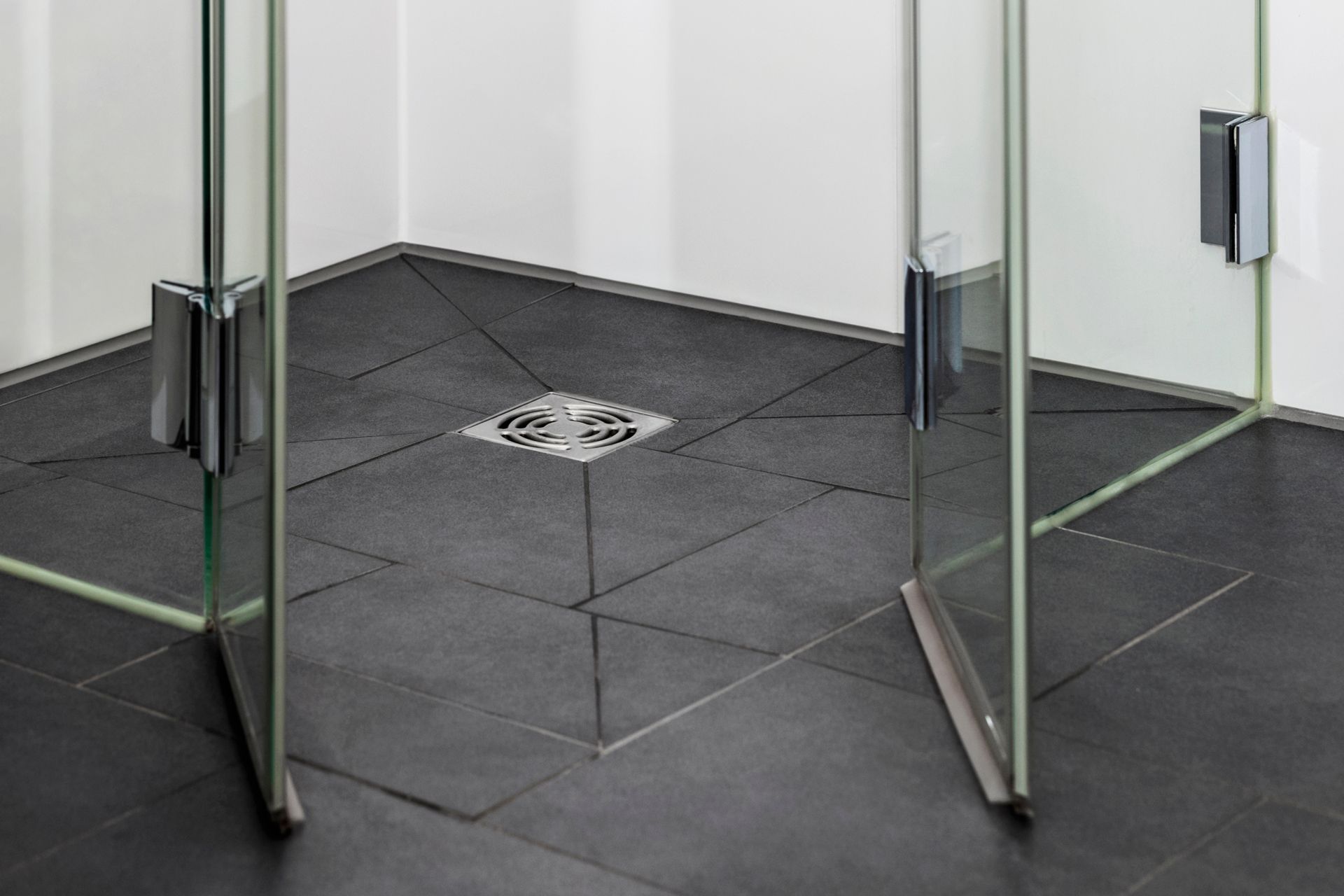 Glass revolving door in a gray-tiled entrance with a floor drain grate.