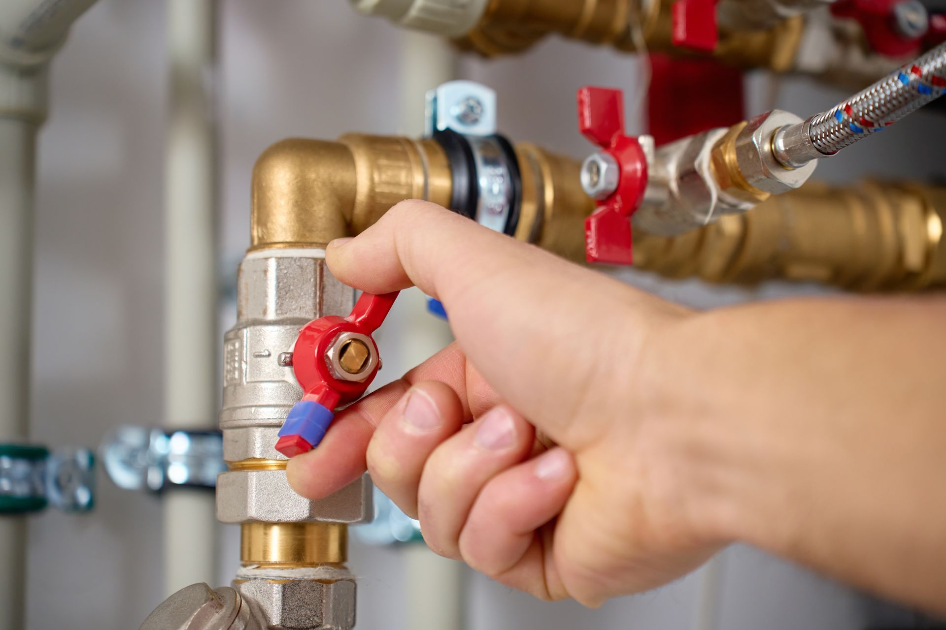 Hand turning a red valve on brass plumbing pipes