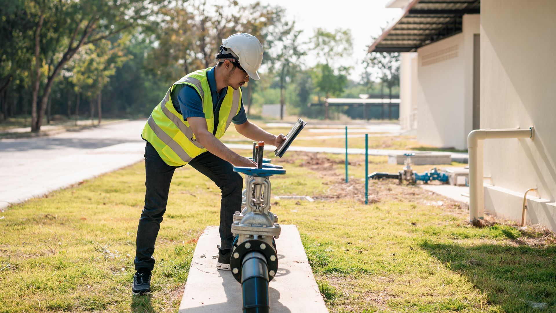 Worker in a reflective vest using a laptop beside a pipeline outdoors
