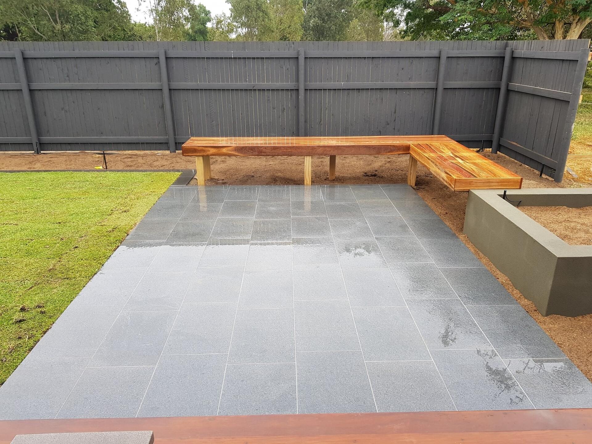 A Wooden Bench is Sitting on a Patio Next to a Fence — Lynams Landscapes Pty Ltd in Jensen, QLD