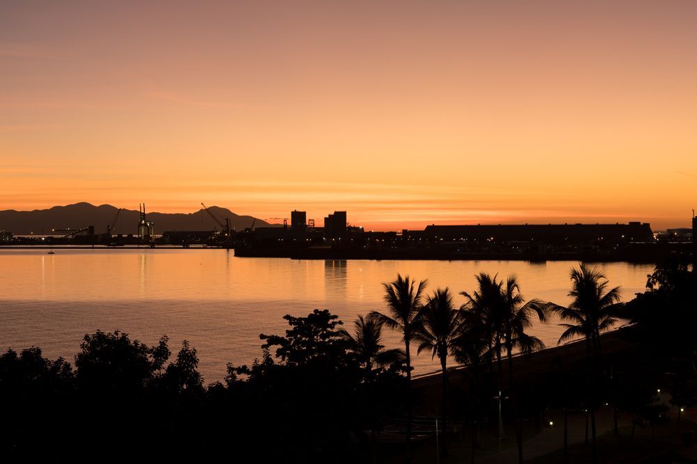A sunset over a body of water with palm trees in the foreground — Lynams Landscapes Pty Ltd in Townsville, QLD