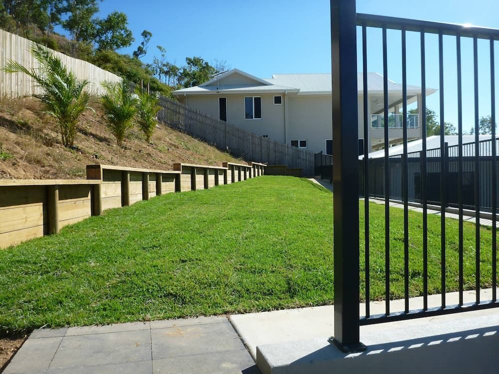 A Fence Surrounds A Lush Green Lawn In Front Of A House — Lynams Landscapes Pty Ltd in Cosgrove, QLD