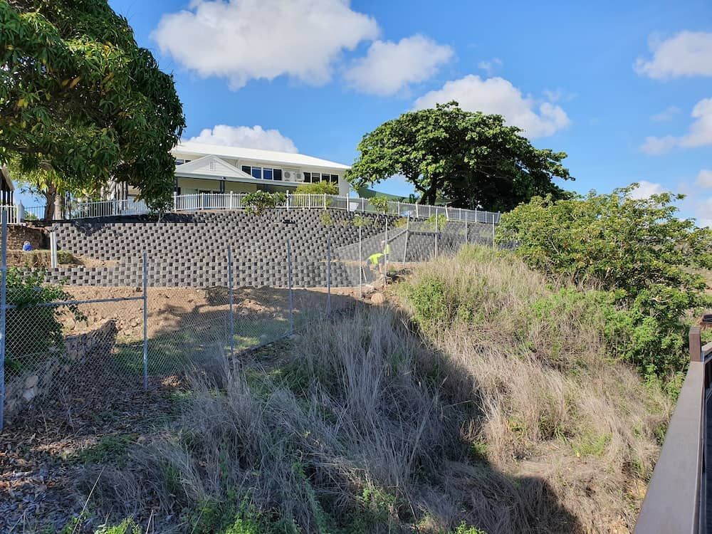 A House is Sitting on Top of a Hill Behind a Chain Link Fence  — Lynams Landscapes Pty Ltd in Cosgrove, QLD