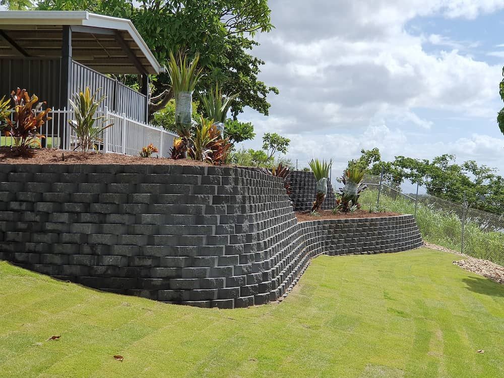 A Large Brick Wall Surrounds a House on a Hillside  — Lynams Landscapes Pty Ltd in Cosgrove, QLD