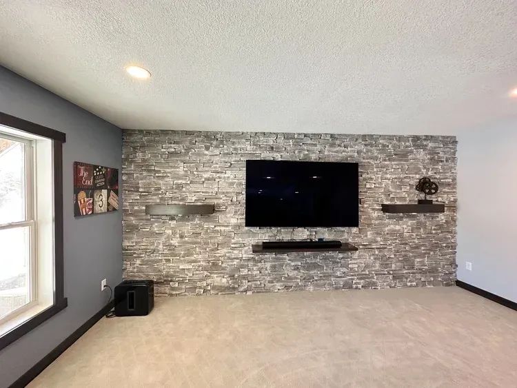Living room with gray stone accent wall, black TV, floating shelves, and black speaker bar.