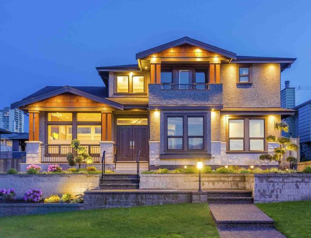 Large modern two-story house at dusk with warm lights, stone exterior, and landscaped front yard Large modern two-story house at dusk with warm lights, stone exterior, and landscaped front yard