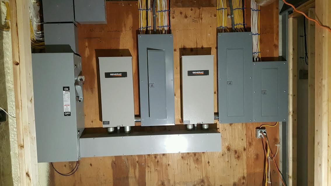 Electrical breaker panel setup on unfinished plywood wall with gray metal boxes and exposed wiring
