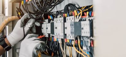 Gloved hands wiring electrical components in a control panel with tangled cables and switches Gloved hands wiring electrical components in a control panel with tangled cables and switches