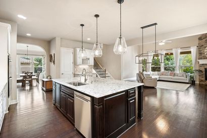 Open-concept kitchen and living room with dark wood floors, white cabinets, and pendant lights Open-concept kitchen and living room with dark wood floors, white cabinets, and pendant lights