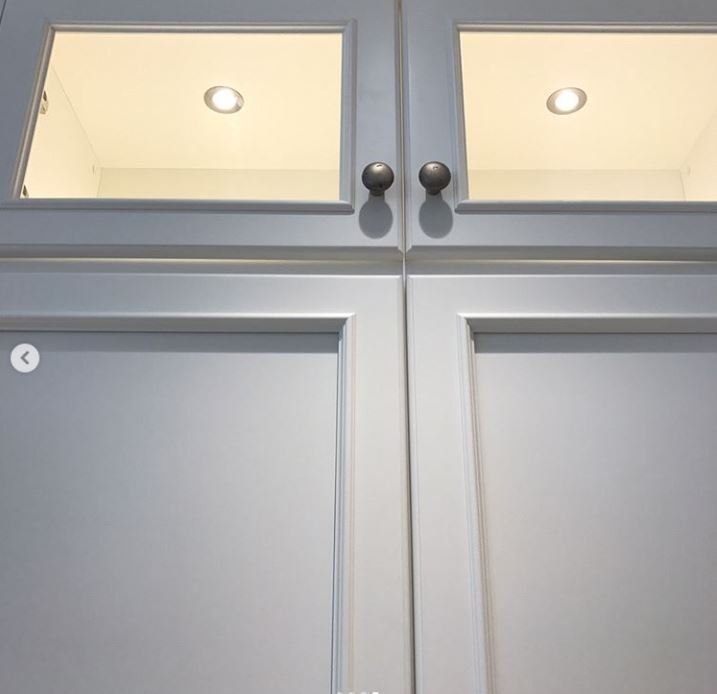 Gray kitchen cabinets with glass upper doors and round black knobs lit from above