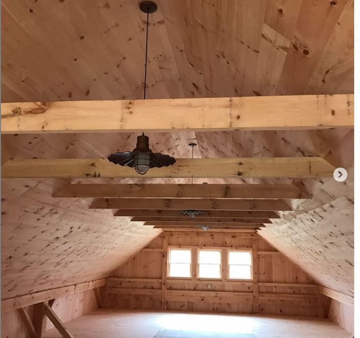 Wood-paneled attic room with exposed beams, small windows, and a ceiling fan centered overhead