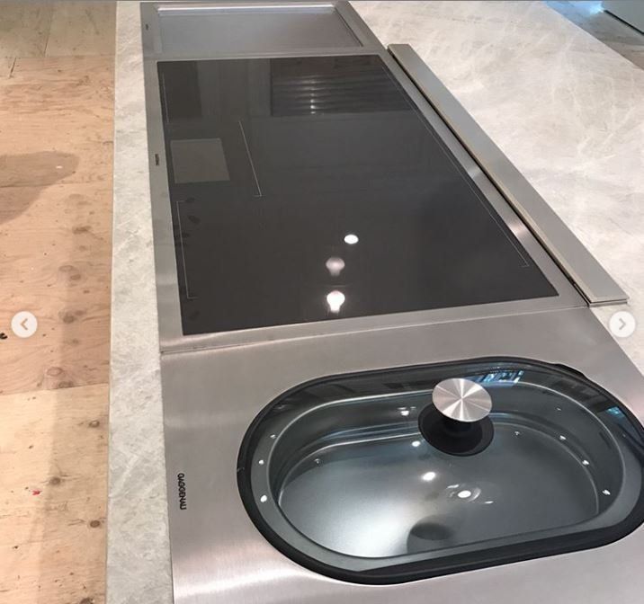 Stainless steel kitchen island with black glass cooktop and oval sink basin with faucet knob