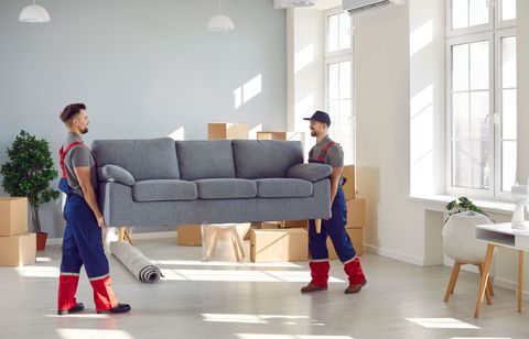 Two men are carrying a couch in a living room.