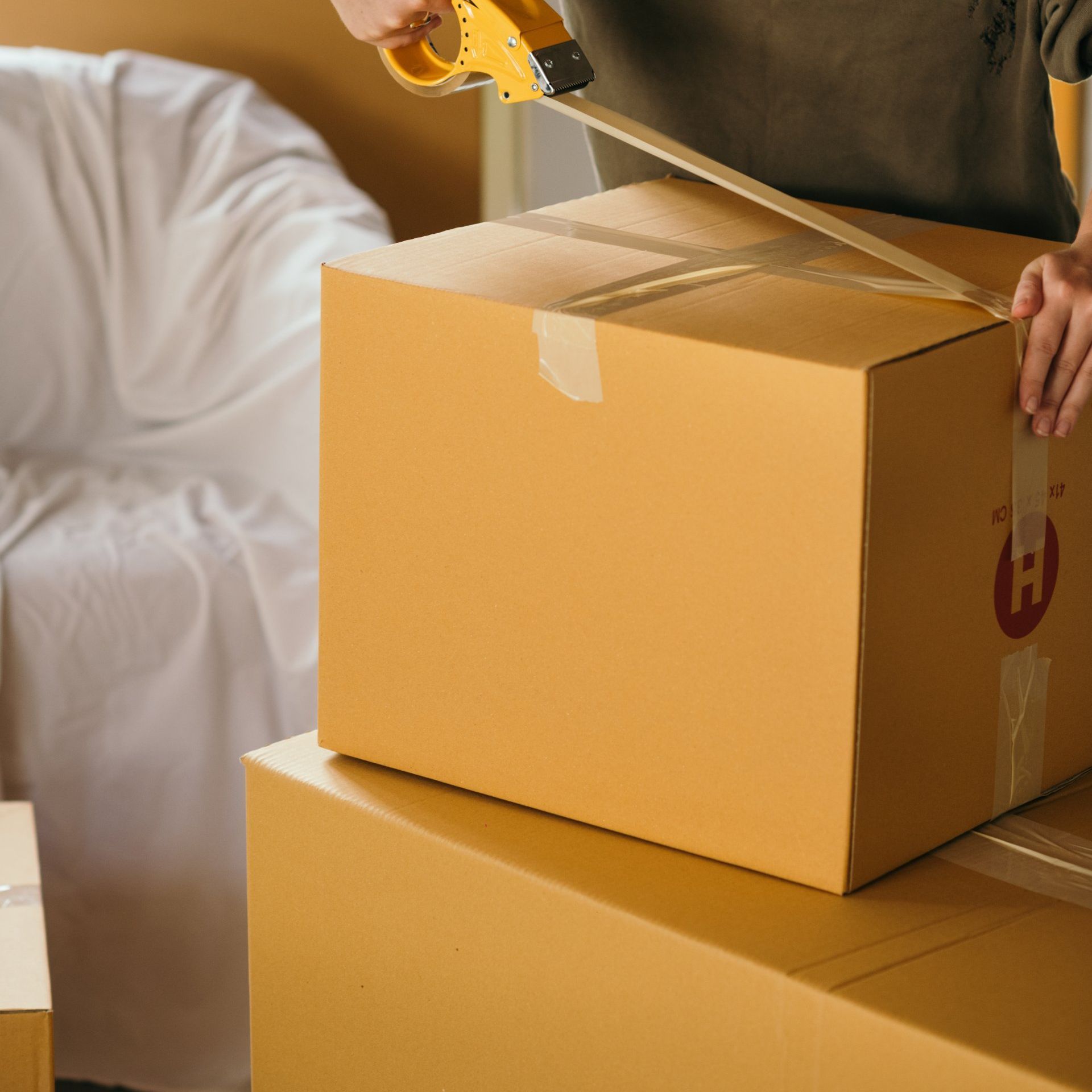 A person is taping a cardboard box with a tape dispenser