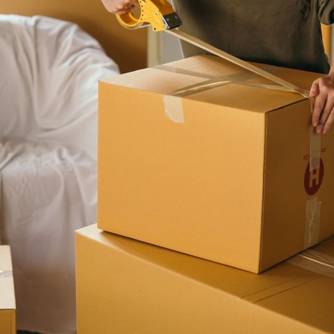 A person is taping a cardboard box with a tape dispenser
