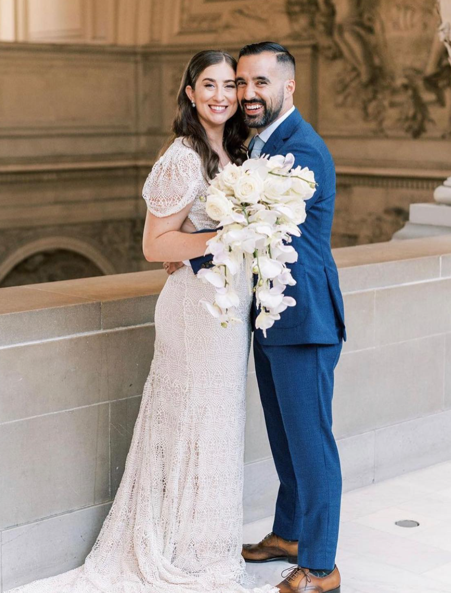 A bride and groom are posing for a picture while the bride is holding a bouquet of flowers.
