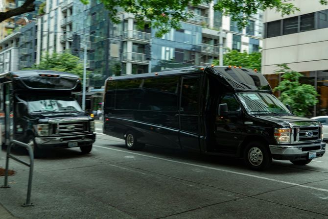 Two black luxury vans parked on a city street beside modern buildings and trees