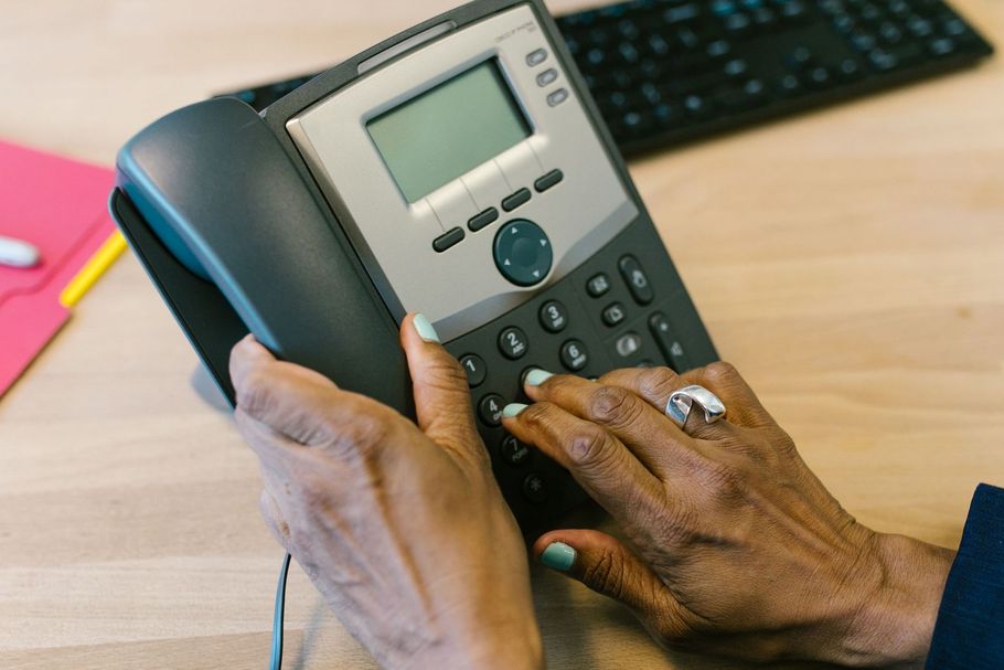 Hands dialing a desk phone on an office desk with a computer keyboard in the background