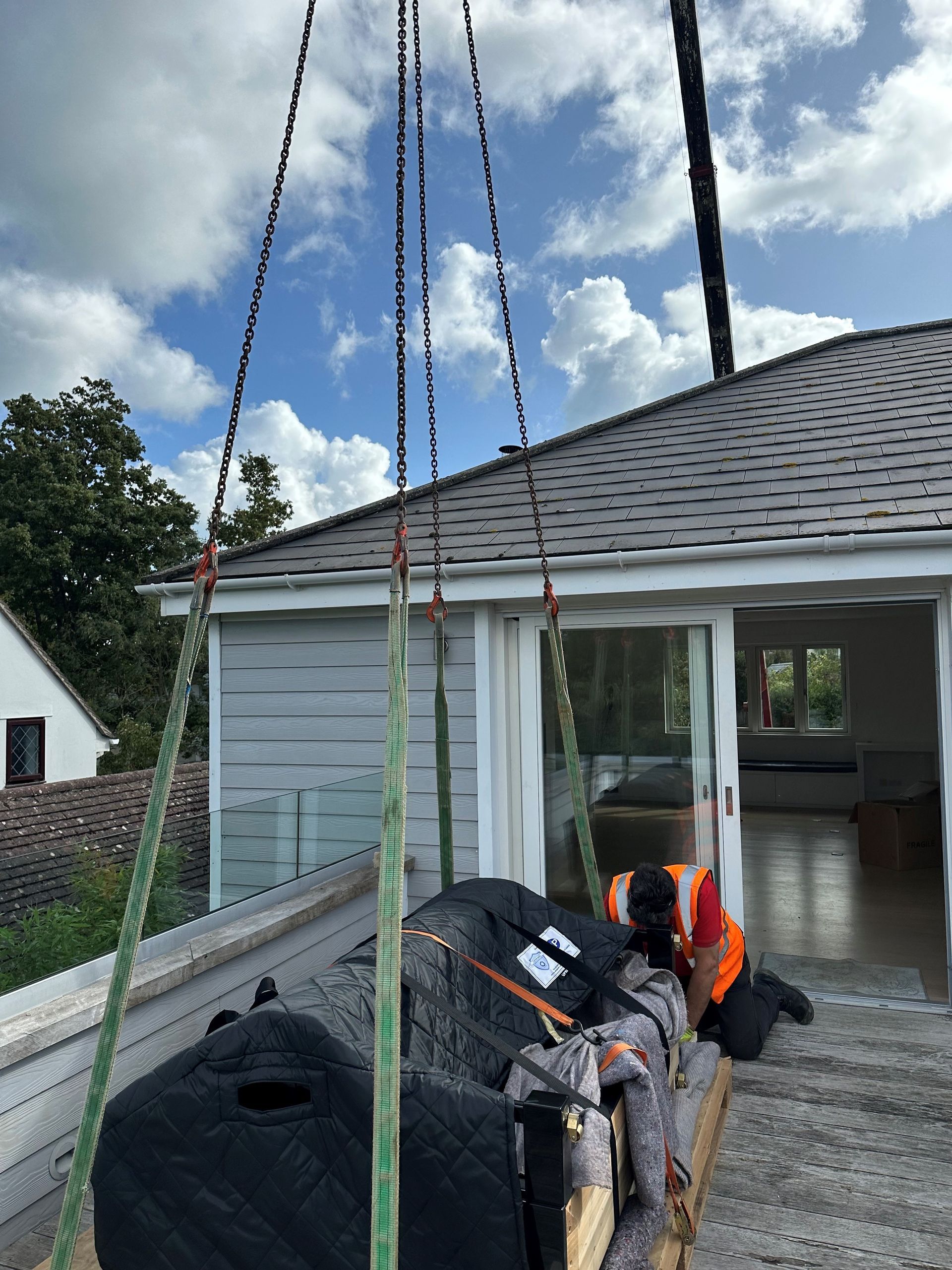 A crane lifting wrapped furniture onto a rooftop deck; construction worker nearby; cloudy sky.